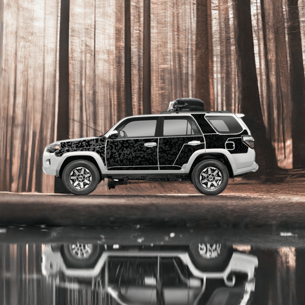 Toyota 4Runner with MEK removable trail armor in black camo design, parked in a forest setting with a reflective water surface.